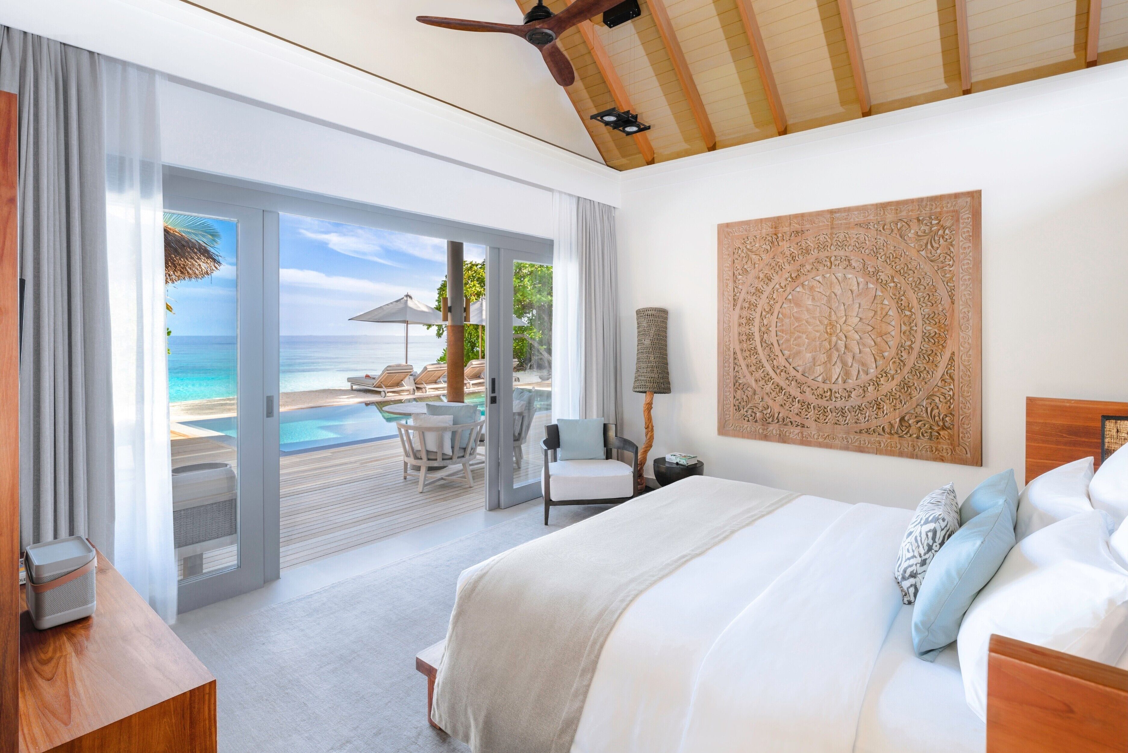 A hotel room with a large bed, a view of the ocean, a ceiling fan, and a wooden ceiling.
