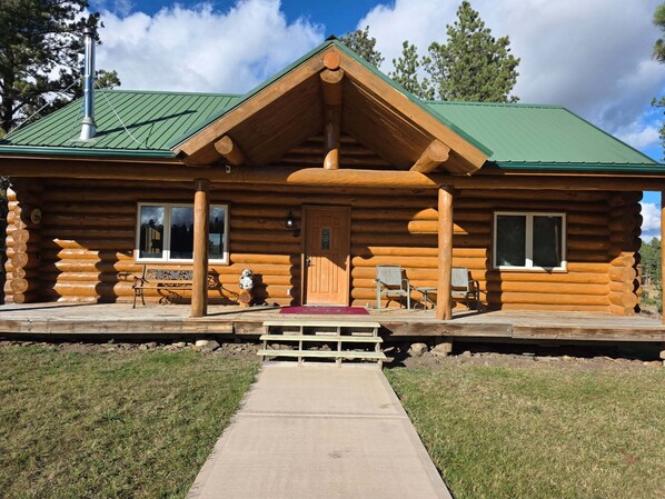 A log cabin with a green roof, a porch with two chairs, and a bench. - Family Friendly 4BR, 3 Bath Cabin w/Hot Tub in the heart of the Black Hills (Hill City)