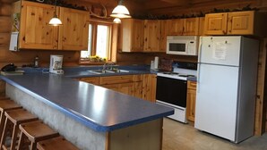 A kitchen with wooden cabinets, a blue countertop, a stainless steel refrigerator, a microwave, a stove, and a coffee maker.