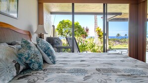 A bedroom with a large bed, a view of the outdoors, and a window with curtains.
