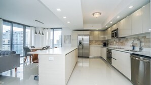 A modern kitchen with a central island, stainless steel appliances, and a large window offering a city view. - New luxurious 3bdr condo at BW with Resort amenities & Beach Chairs  (Hallandale Beach)