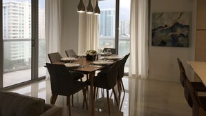 A modern dining area with a large table set for six, large windows with curtains, and a city view. - New luxurious 3bdr condo at BW with Resort amenities & Beach Chairs  (Hallandale Beach)