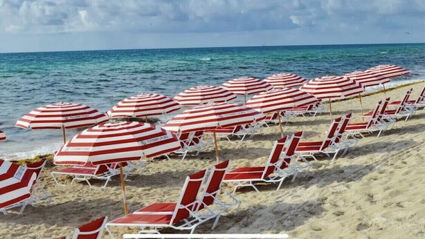 A beach with rows of red and white striped beach umbrellas and white lounge chairs. - New luxurious 3bdr condo at BW with Resort amenities & Beach Chairs  (Hallandale Beach)