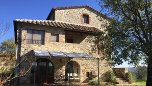 A stone building with a tiled roof, a covered patio, and a garden.
