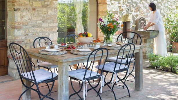 An outdoor patio with stone walls, a table set for dining, and a person at a counter.