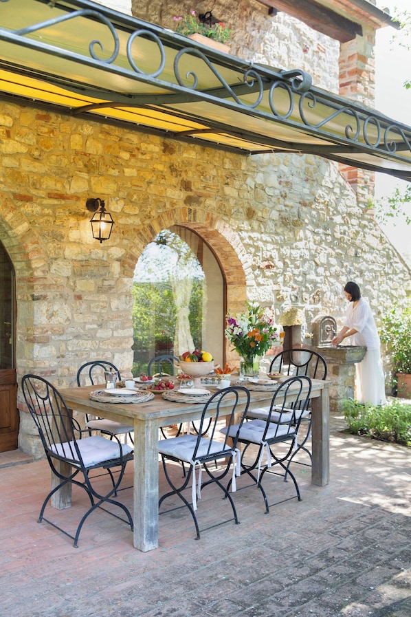 Eine Terrasse im Freien mit Steinmauern, einem Esstisch und einer Person an einer Theke.