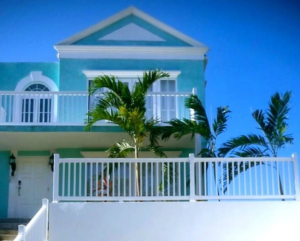 A two-story building with a balcony, a white fence, and a clear blue sky. - 'Sunset Vista' - Negril Seafront Townhouse - W/Solar Power (Negril)