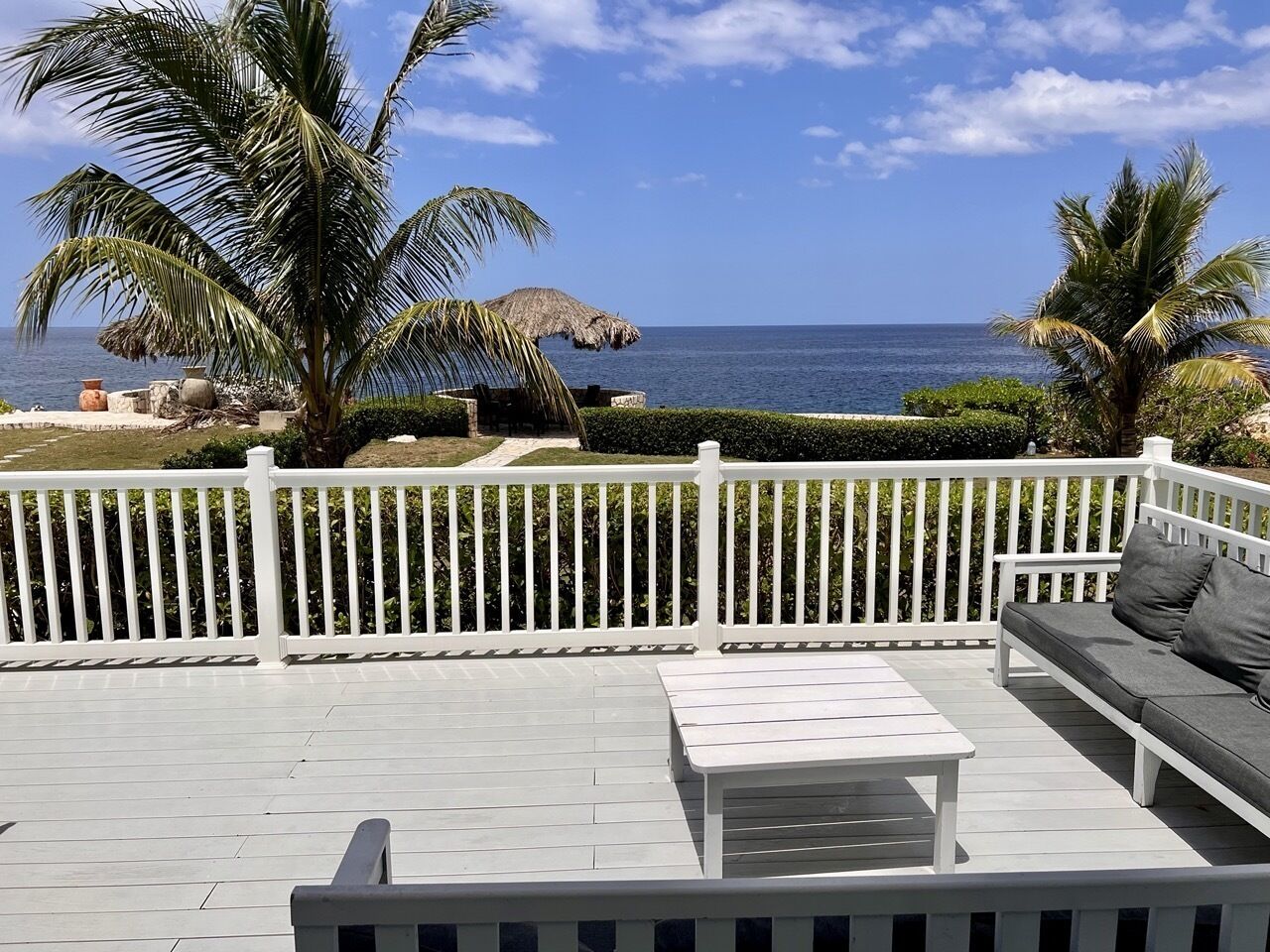 A deck with a white fence, a white table, and a gray sofa with cushions.