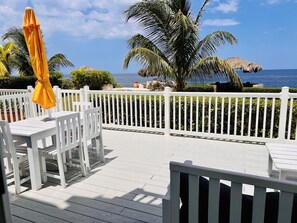 An outdoor deck with white railings and tables, overlooking a beach with palm trees and a clear sky. - 'Sunset Vista' - Negril Seafront Townhouse - W/Solar Power (Negril)