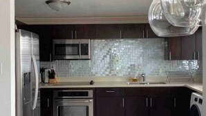 Une cuisine moderne avec des meubles de couleur sombre, des appareils en acier inoxydable, un dosseret carrelé et un luminaire suspendu.