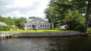 Ein Haus am See mit einer Anlegestelle, umgeben von Bäumen und einem roten Fahrzeug.
