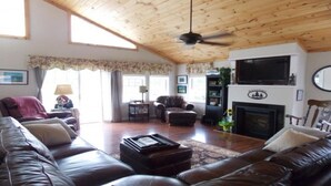 Ein geräumiges Wohnzimmer mit Holzboden, Ledersofas, Kamin und Fernseher.