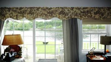 A room with a view of a lake, a table with a lamp, and a chair by the window.