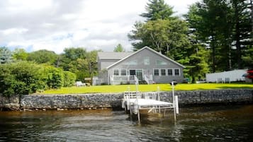 A house with a dock extending into a body of water, surrounded by greenery and trees.