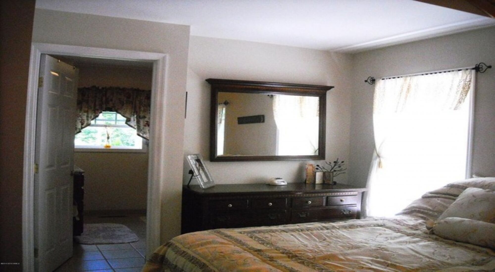 Une chambre à coucher avec un lit, une commode, un miroir et une fenêtre avec des rideaux.
