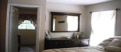 Une chambre à coucher avec un lit, une commode, un miroir et une fenêtre avec des rideaux.