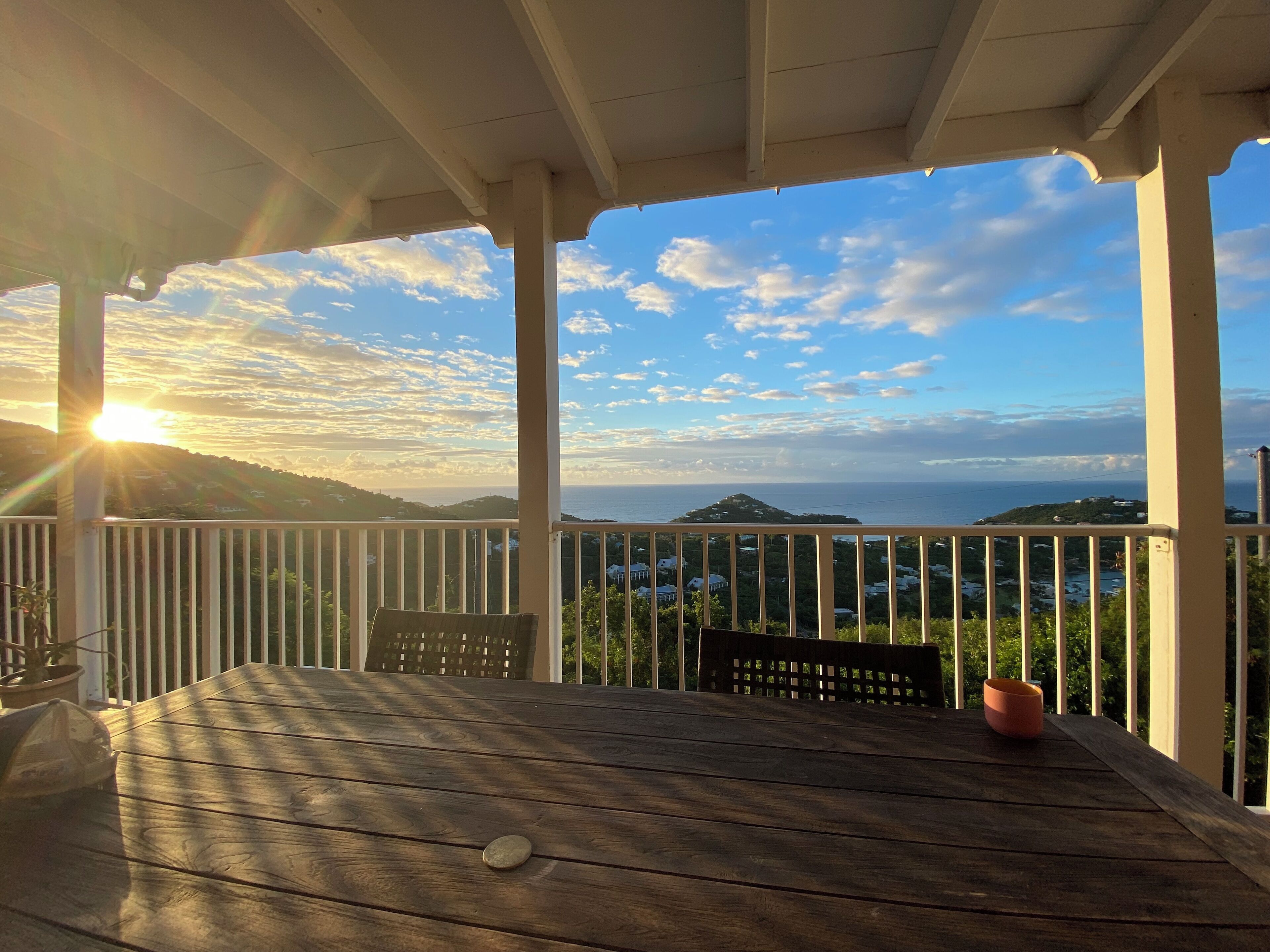 Eine Holzdar Terrasse mit Tisch und Stühlen, mit Blick auf eine Küstenlandschaft mit Hügeln und dem Meer.