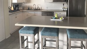 Une cuisine avec des armoires blanches, un réfrigérateur en acier inoxydable, un four à micro-ondes et un grand îlot central doté de tabourets de bar.