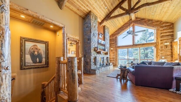 A spacious log cabin interior with a stone fireplace, wooden floors, and a large window offering a view of the outdoors. - Views! Space! Featured on CBS Staycation Luxury Big Bear Pool Table & Theater (Big Bear Lake)