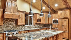 A kitchen with wooden cabinets, a granite countertop, a central island, stainless steel appliances, and pendant lighting. - Views! Space! Featured on CBS Staycation Luxury Big Bear Pool Table & Theater (Big Bear Lake)