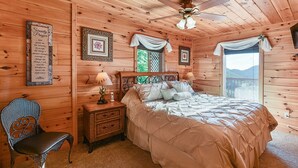 Um quarto acolhedor de madeira, com uma cama, uma mesinha de cabeceira, uma cadeira e um ventilador de teto.
