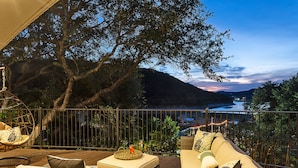 A balcony with wicker furniture, a hanging chair, and a view of a lake at dusk. - Lakefront/Pool & Hot Tub/NEW PICKLEBALL/Sand Volley Ball/4 acres/Sleeps 28 (Austin)