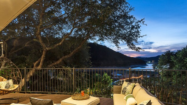 A balcony with wicker furniture, a hanging chair, and a view of a lake at dusk. - Lakefront/Pool & Hot Tub/NEW PICKLEBALL/Sand Volley Ball/4 acres/Sleeps 28 (Austin)