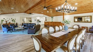 A spacious living room with a wooden ceiling, a dining area with a large wooden table, and a kitchen in the background. - Lakefront/Pool & Hot Tub/NEW PICKLEBALL/Sand Volley Ball/4 acres/Sleeps 28 (Austin)
