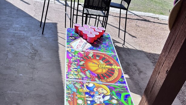 A long table with a colorful, illustrated design, placed on a concrete surface outdoors. - Lakefront/Pool & Hot Tub/NEW PICKLEBALL/Sand Volley Ball/4 acres/Sleeps 28 (Austin)