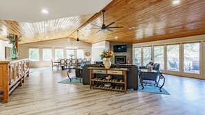 A spacious living room with a wooden ceiling, a central island with a sink, a dining area with chairs, and large windows. - Lakefront/Pool & Hot Tub/NEW PICKLEBALL/Sand Volley Ball/4 acres/Sleeps 28 (Austin)