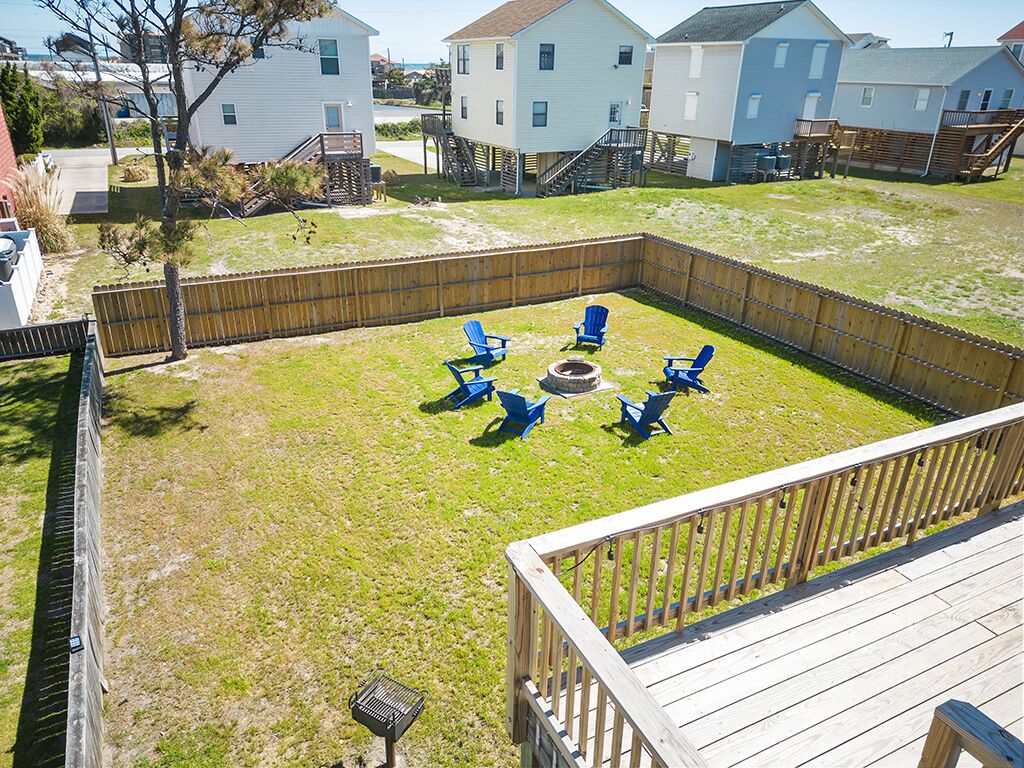 A backyard with a wooden deck, a fire pit, and blue chairs arranged around it.
