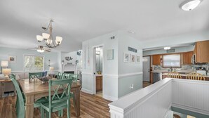 A spacious dining area with a wooden table and green chairs, a kitchen with wooden cabinets, and a ceiling fan.