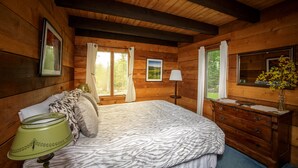 A wooden cabin bedroom with a bed, dresser, and two windows with curtains. - Reillys Rest-private home in Green Mtns, kid-pet friendly-Ski,Bike,Walk,Relax! (Weston)