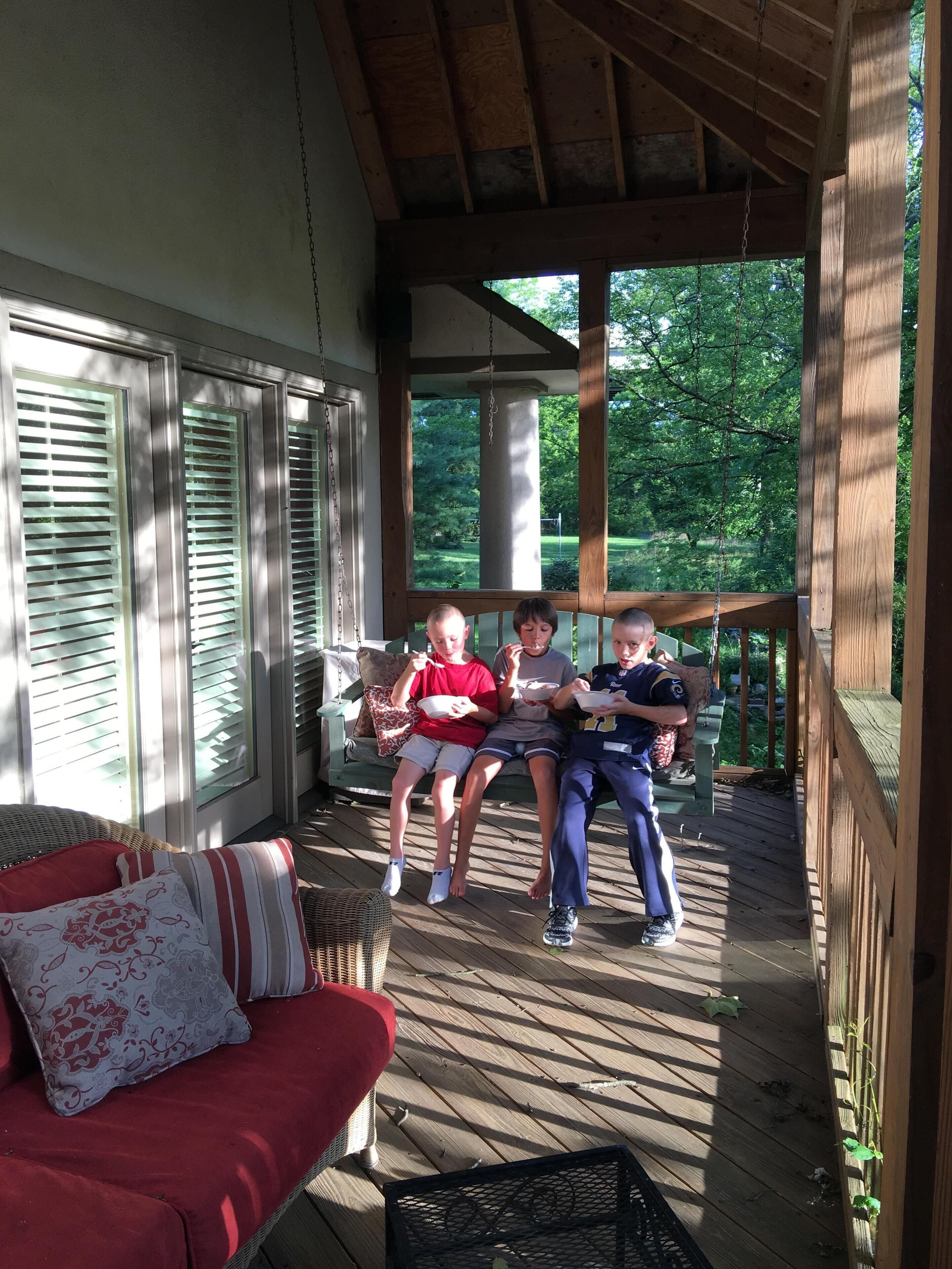 A covered porch with a wooden floor, a red cushioned sofa, and a wicker chair.