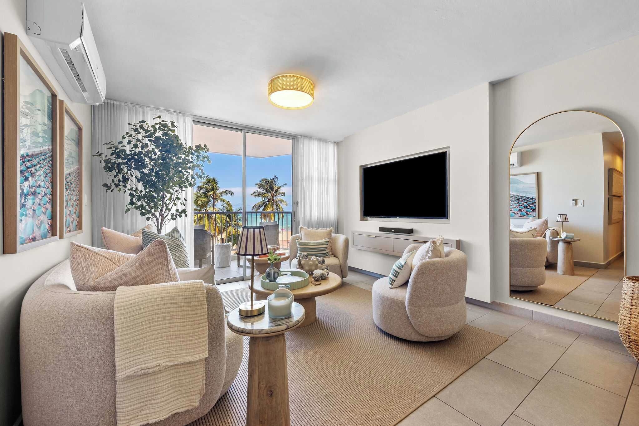A modern living room with a large TV, comfortable seating, a balcony with a view, and a large mirror.