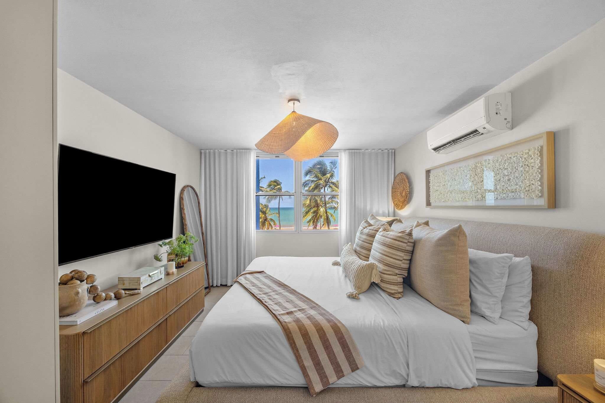 Un dormitorio moderno con una cama grande, un televisor de pantalla plana, un aparador de madera y vista a la playa.