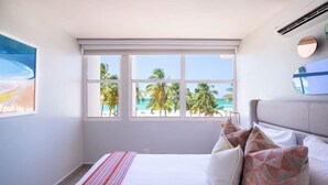 Ein Schlafzimmer mit einem großen Fenster und Blick auf Palmen und den Strand.