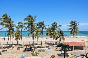 Vista de la playa con palmeras, un área cercada y un edificio con techo rojo.
