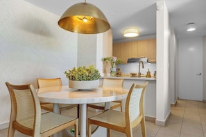 A dining area with a round table, four chairs, a central plant, and a pendant light.