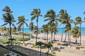 A beach with palm trees, a fence, and a clear view of the ocean.