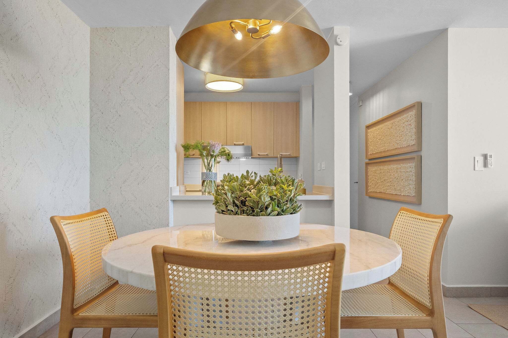 Un coin repas avec une table ronde, deux chaises, une plante placée au centre et un luminaire suspendu.
