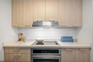 A modern kitchen with wooden cabinets, a stainless steel range hood, a double oven, and a white countertop.