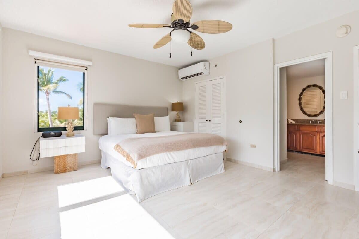 A bedroom with a bed, a ceiling fan, a window, an air conditioning unit, and a view of the outdoors.