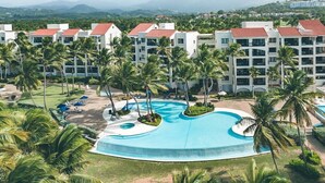 Un resort con una amplia piscina rodeada de palmeras y vistas a montañas distantes.
