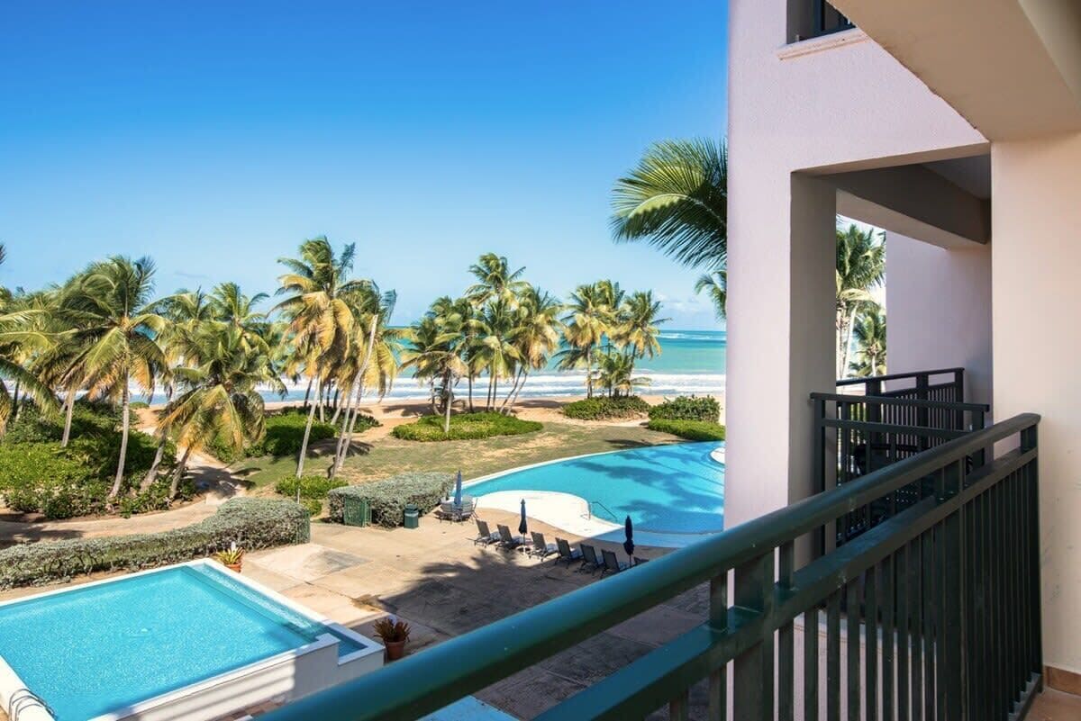A pool area with a view of the beach and palm trees.