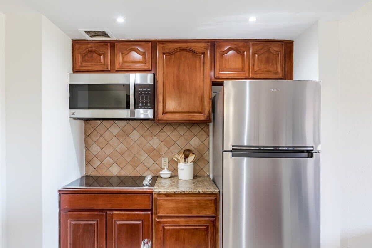 A kitchen with wooden cabinets, a stainless steel refrigerator, a microwave, and a tiled backsplash.
