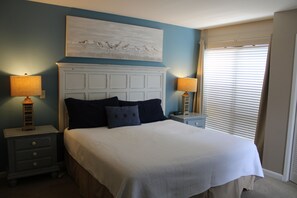 A bedroom with a large bed, two bedside tables with lamps, a white headboard, and a painting above the bed. - Casual, clean, comfy, beautiful views. Golf cart with agreement. Love your stay. (Miramar Beach)