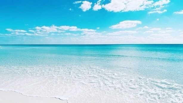 Une plage à l’eau turquoise et au sable blanc.