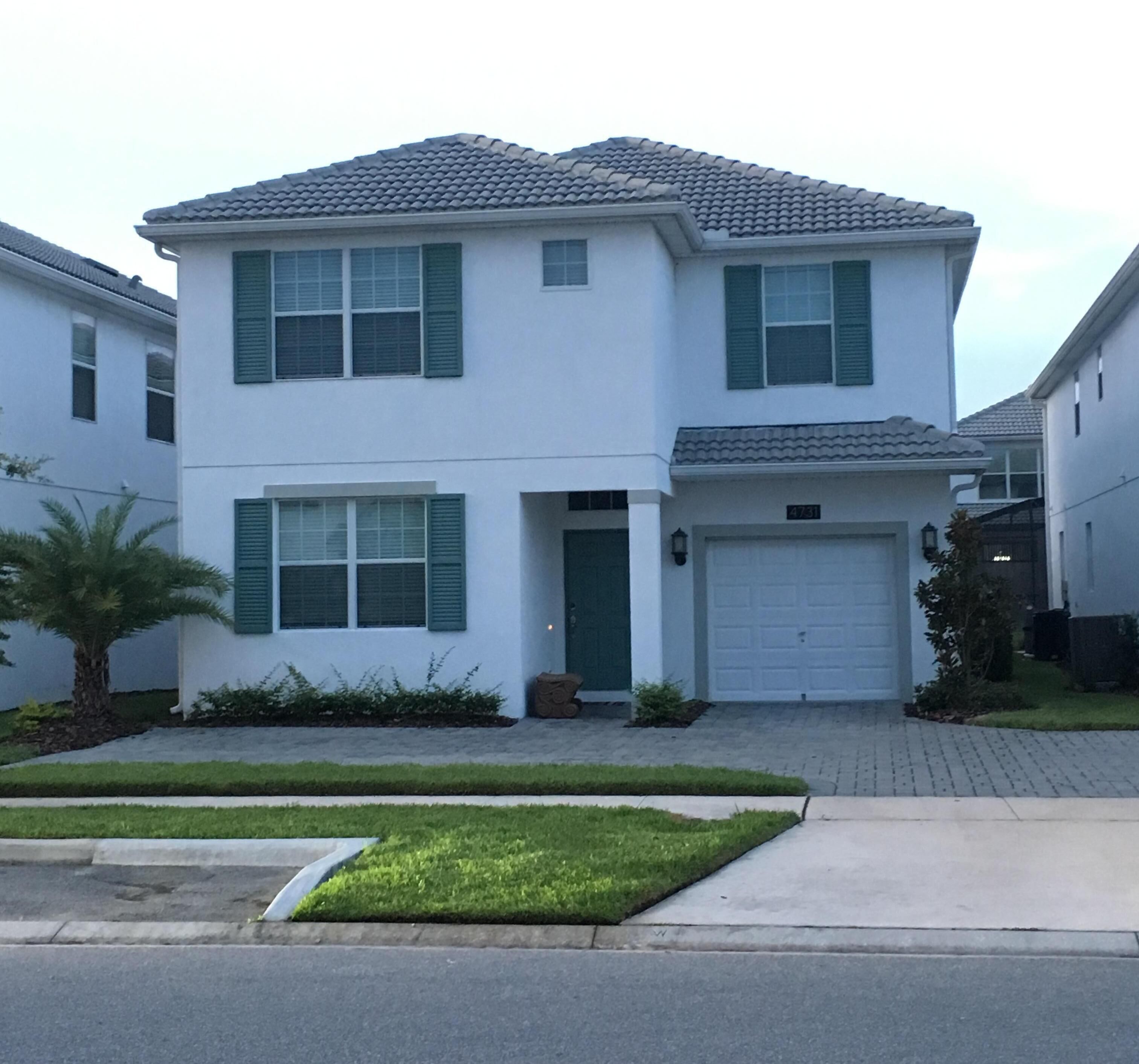 A two-story residential building with a garage, green shutters, and a well-maintained lawn.