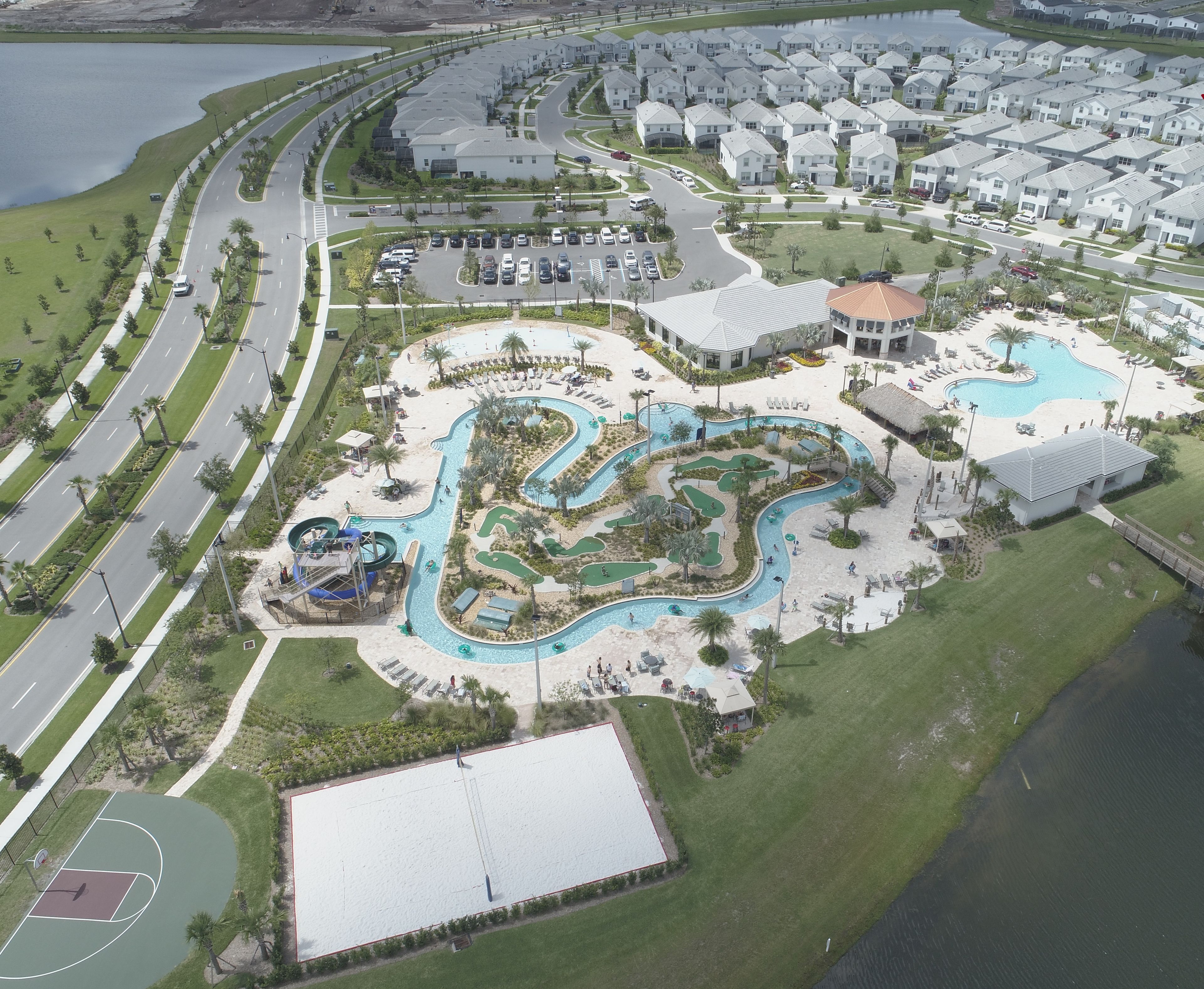 Vista aérea de una zona residencial con una amplia piscina, un campo de golf y una cancha de baloncesto.